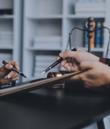 Business and lawyers discussing contract papers with brass scale on desk in office. Law, legal services, advice, justice and law concept picture with film grain effect